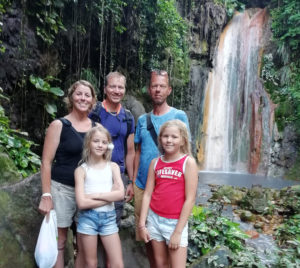 Tre vuxna och två barn står framför ett vattenfall och ler.