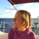 En kvinna med blont hår sitter på en båt och tittar ut mot horisonten.